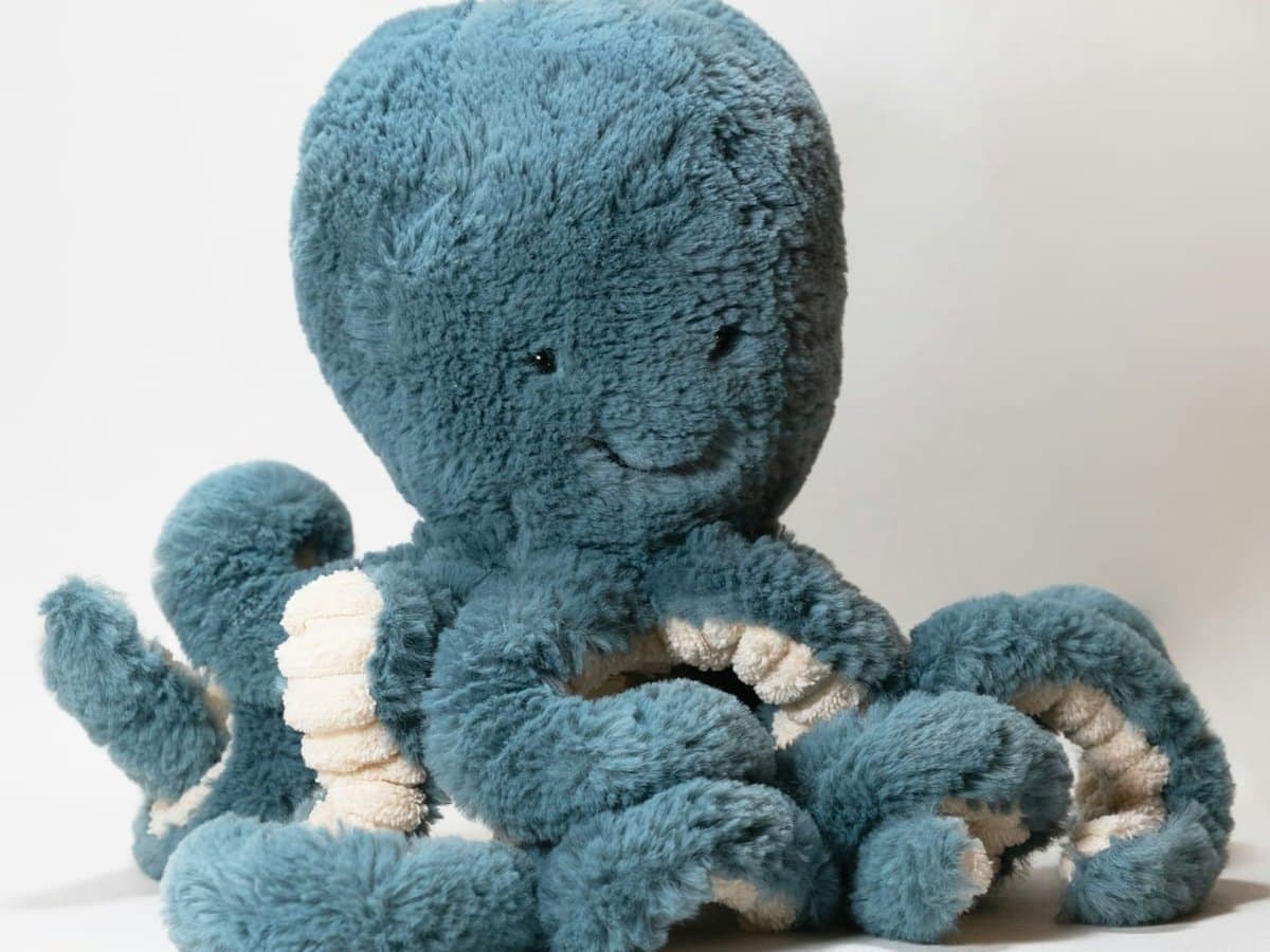 A teal-blue plush octopus with cream sucker rows, sitting on a pale ground.
